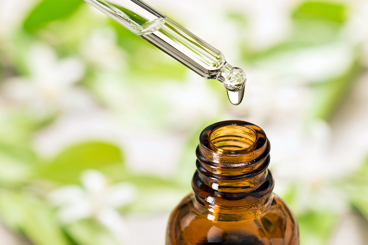 Essential oil falling from glass dropper into brown glass bottle